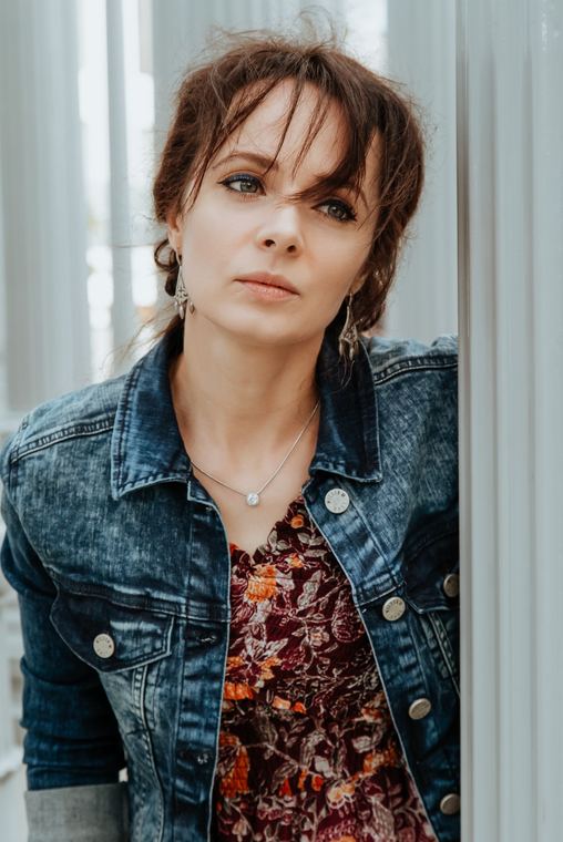 Olya in a denim jacket leaning in a doorway