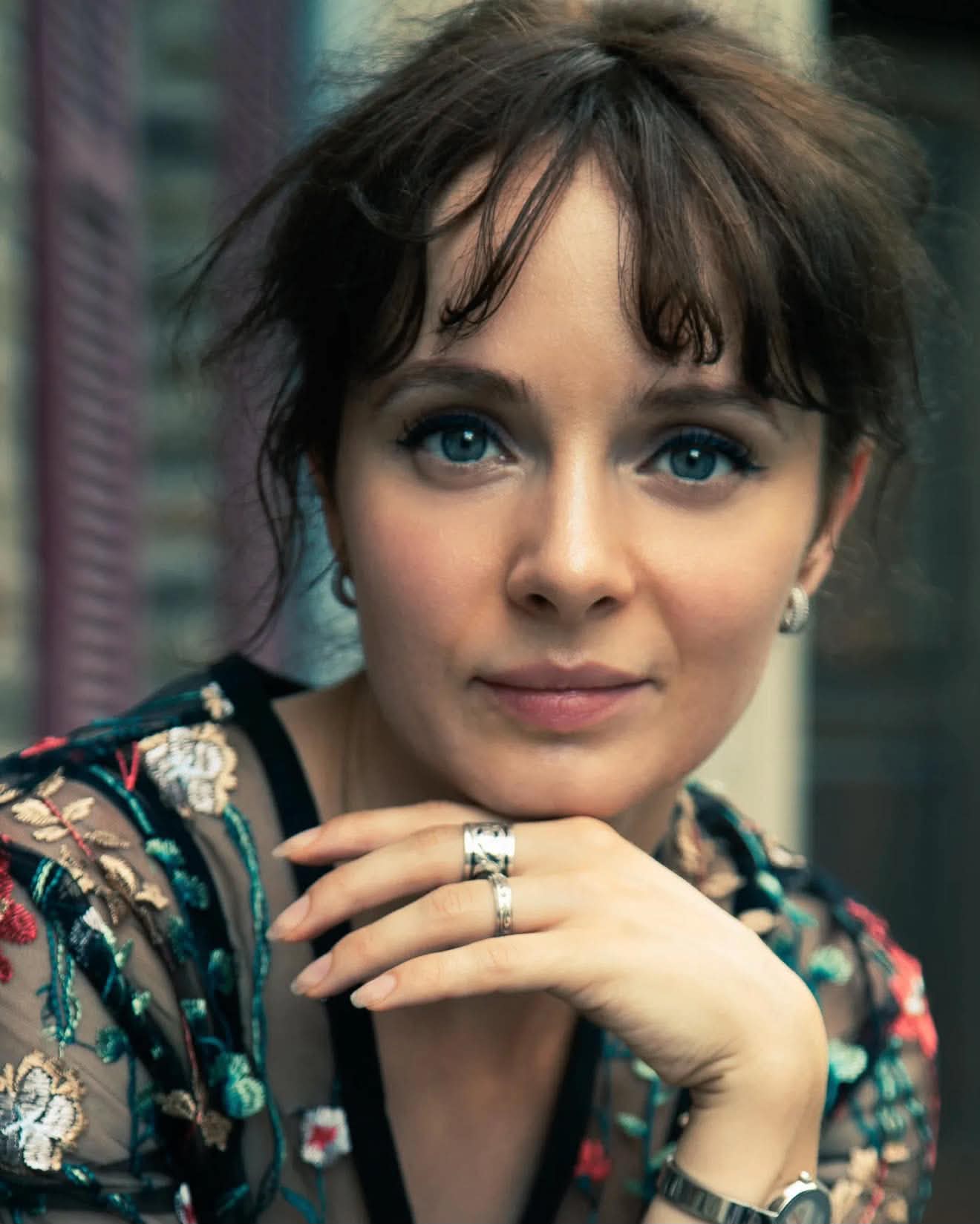 Olya Aman in an embroidered floral top, chin resting on her hand